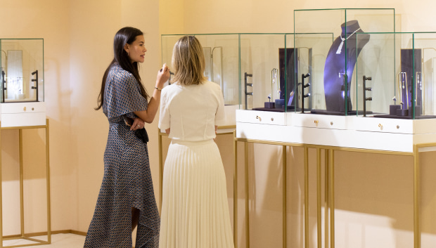Two women engaged in a discussion while observing jewellery in a display case, highlighting their interest in the pieces.