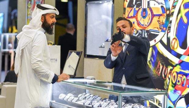 A man in a suit examines a watch while standing in a store, showcasing his interest in luxury timepieces.