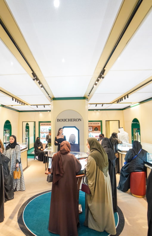 A diverse group of individuals examines various jewellery items displayed in a booth, showcasing their interest in these items.