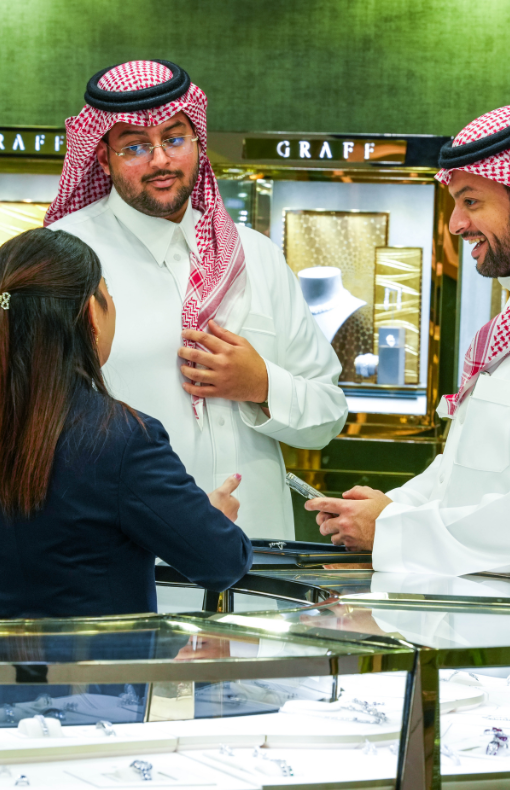 A woman speaks with two men in traditional Middle Eastern clothing at a Graff jewellery booth.