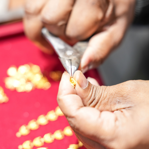 Jeweller holding a small gold piece with tweezers over a red display tray.